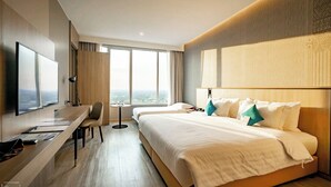 Ein Hotelzimmer mit einem großen Bett, einem Schreibtisch mit Stuhl, einem Fernseher und Blick auf die Stadt durch große Fenster.