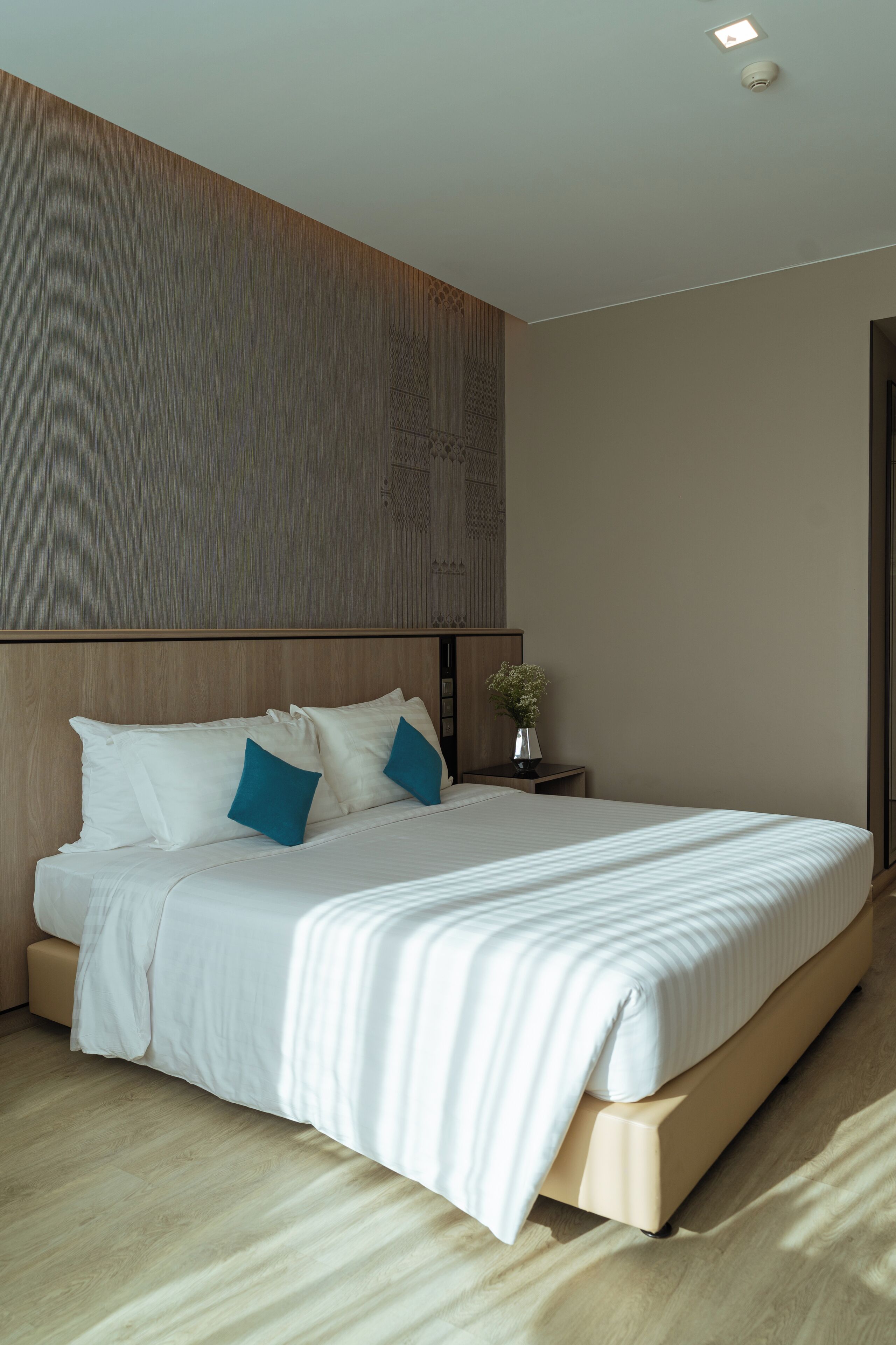 Et moderne hotelværelse med en stor seng, et træhovedgærde og et lille natbord med en vase.