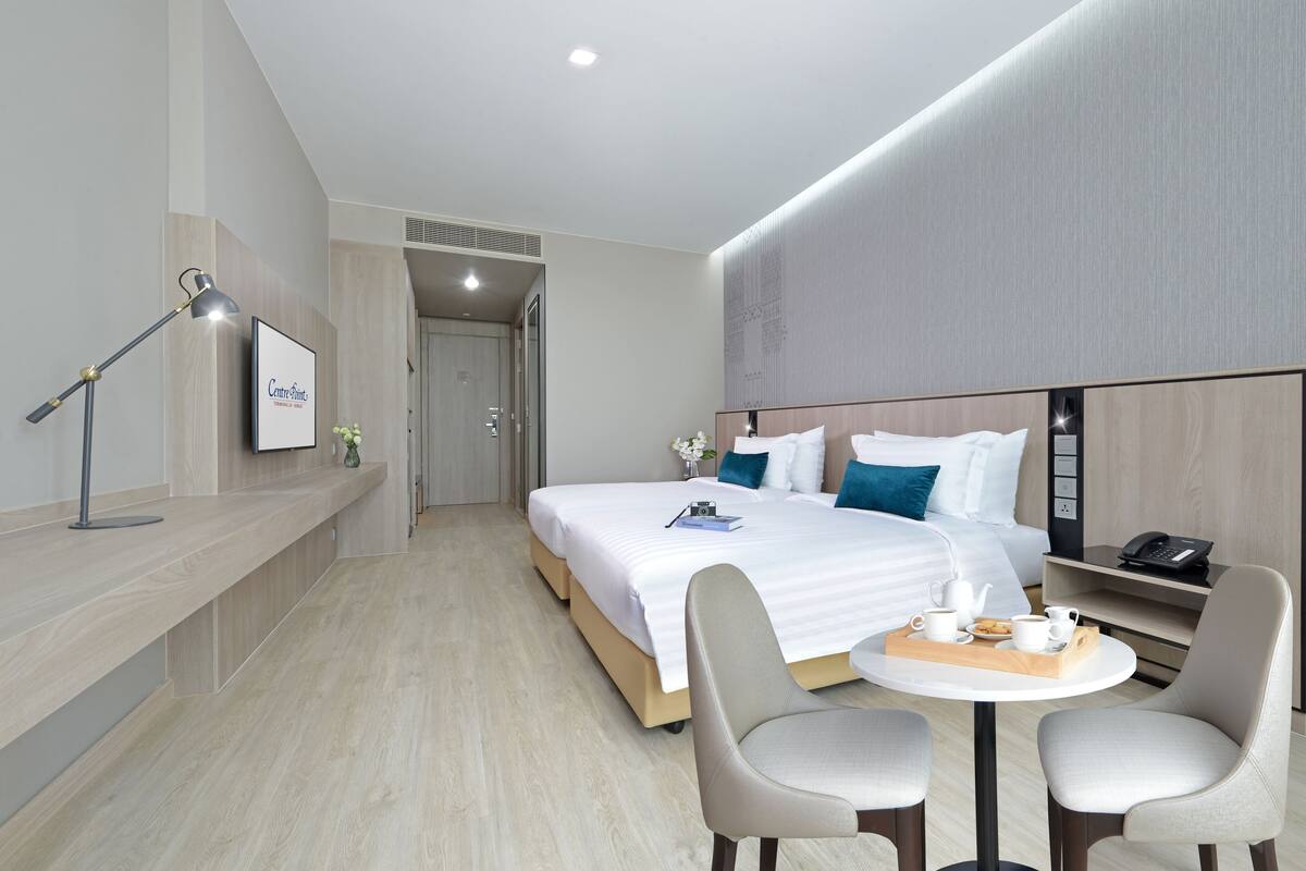 A modern hotel room with a large bed, bedside table, and a small round table with chairs.