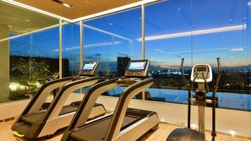 A gym with treadmills and an elliptical machine, large windows with a city view, and a wooden floor.