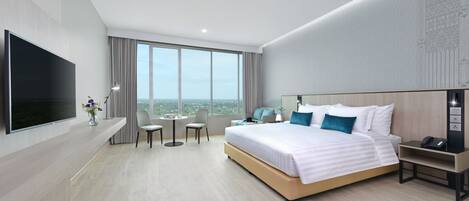 A modern hotel room with a large bed, a flat-screen TV, a desk, and a view of the city.