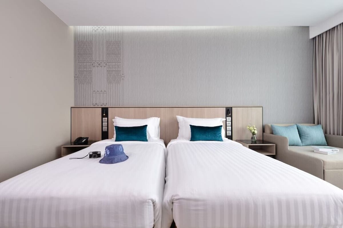 A hotel room with two beds, a sofa, a nightstand, and a wall with a decorative panel.