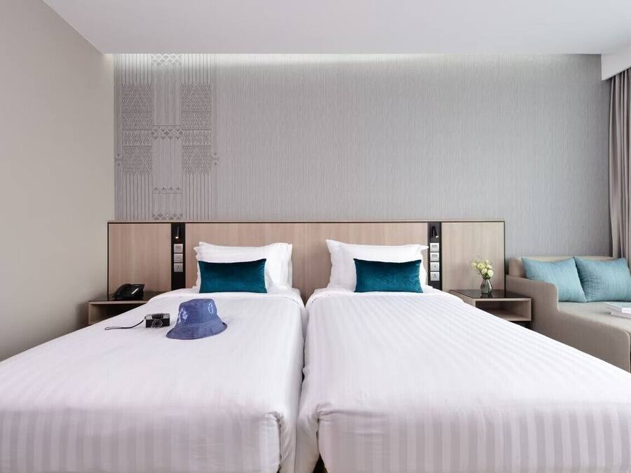 Una habitación de hotel con dos camas, un sofá, una mesita de noche y una pared decorada con un panel.