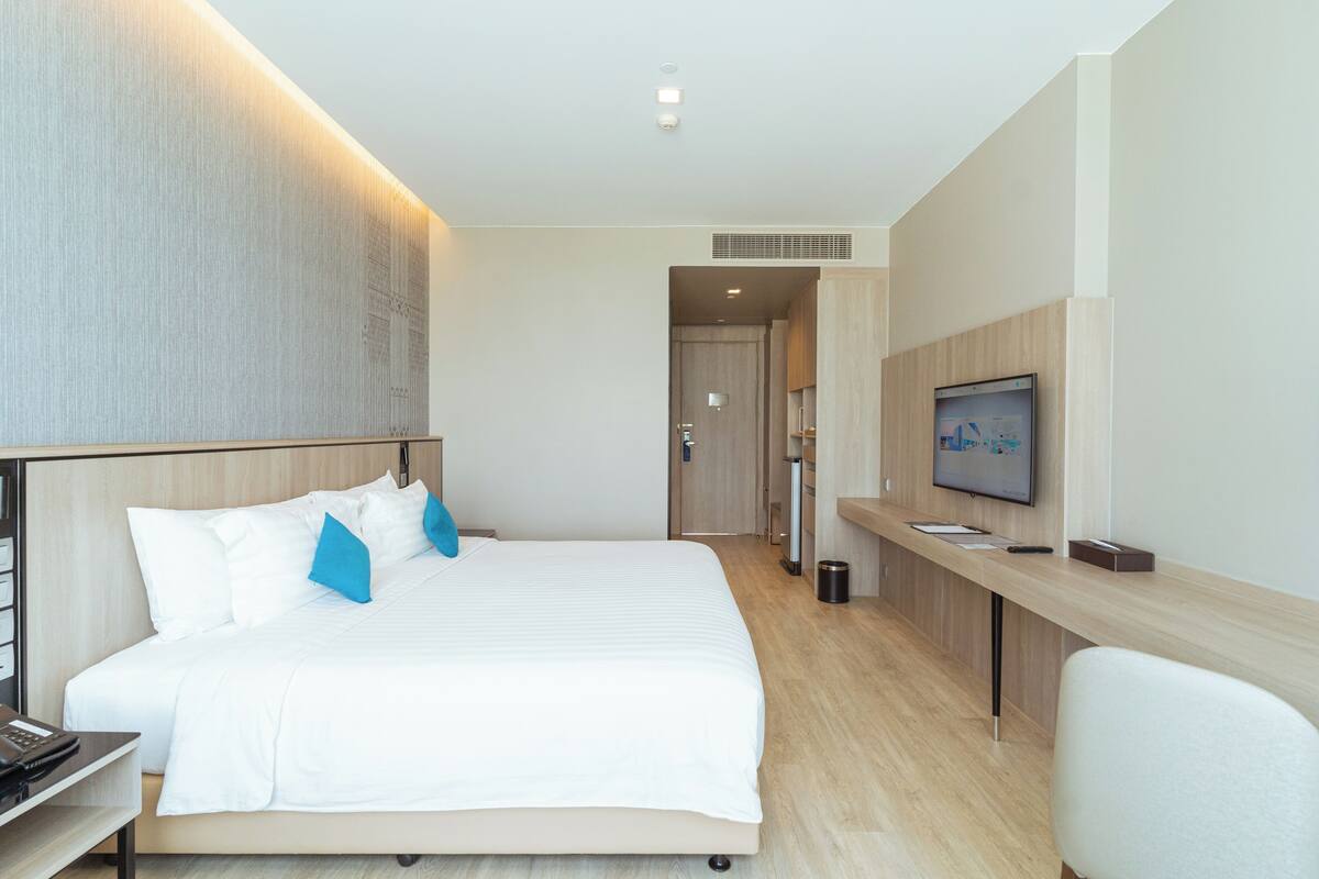 A modern hotel room with a large bed, a desk, and a television.