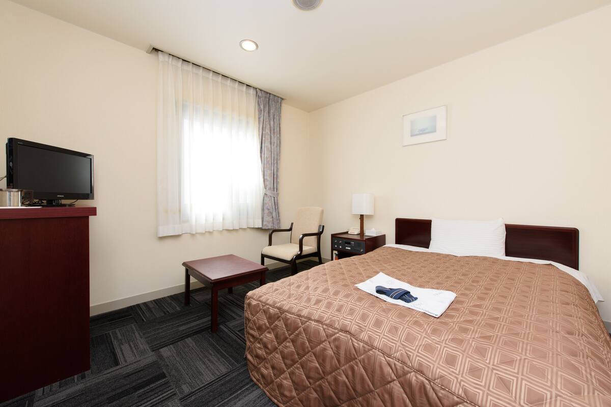 A hotel room with a bed, a desk, a chair, a television, and a window with curtains.