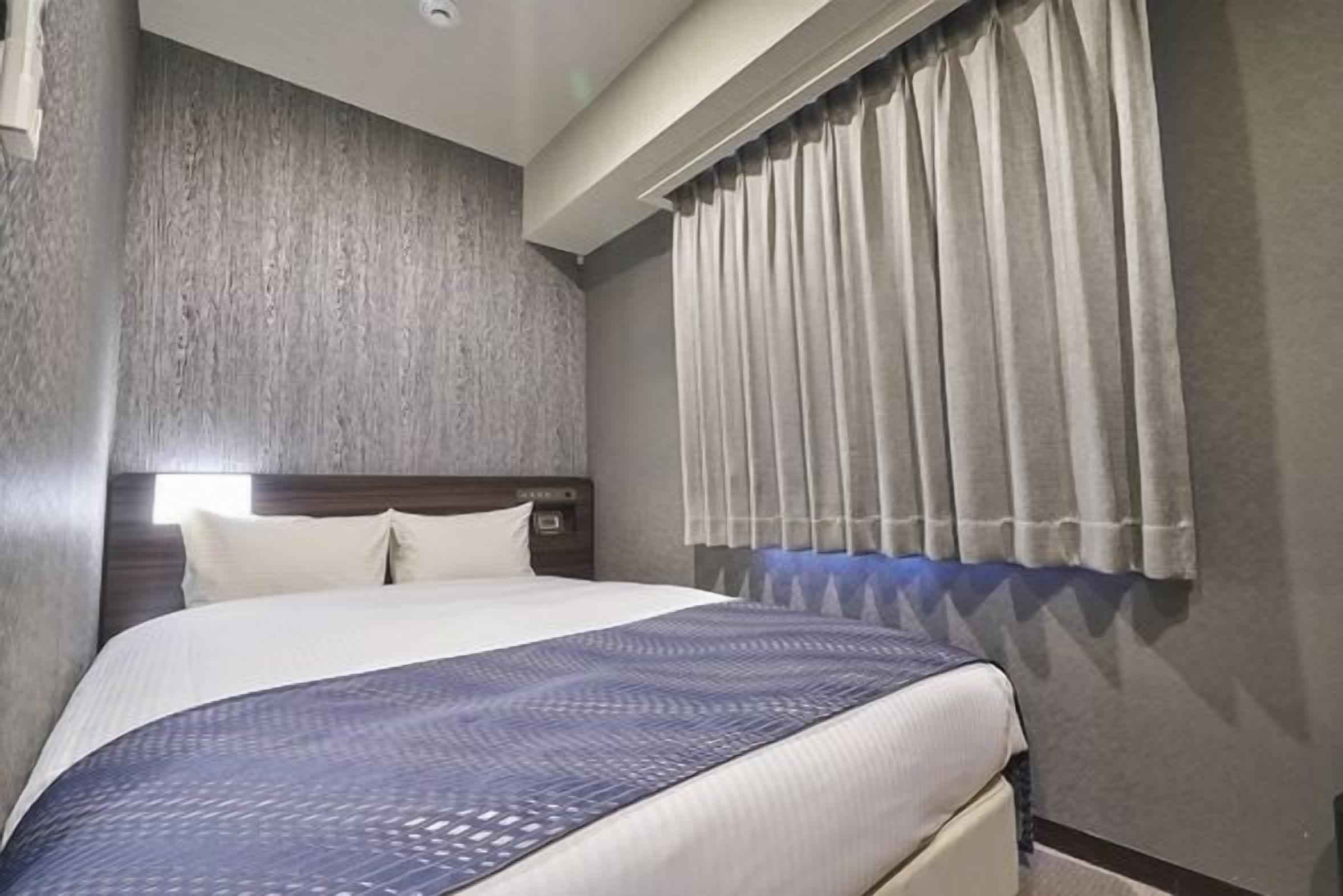 A hotel room with a large bed, a headboard, a window with curtains, and a textured wall.