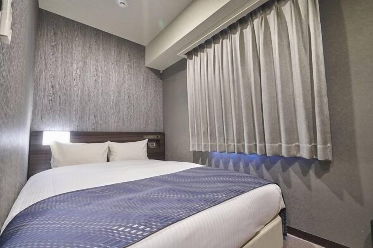Ein Hotelzimmer mit einem großen Bett, einem Kopfteil, einem Fenster mit Vorhängen und einer strukturierten Wand.