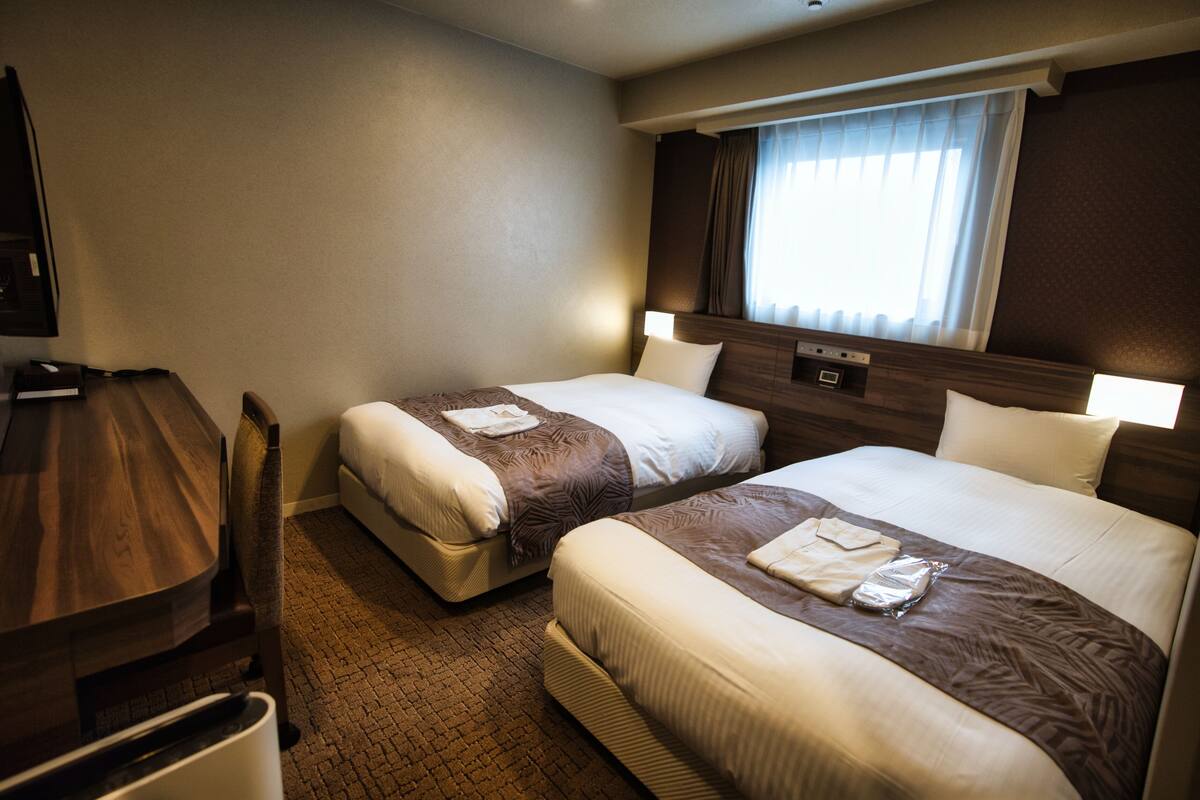 Ein Hotelzimmer mit zwei Betten, einem Schreibtisch und einem fenster mit Vorhängen.