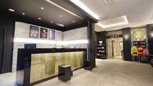A reception area with a modern design, featuring a reception desk, a wall-mounted menu board, and a seating area with plush chairs. - Hotel Vine Osaka Kitahama (Osaka)