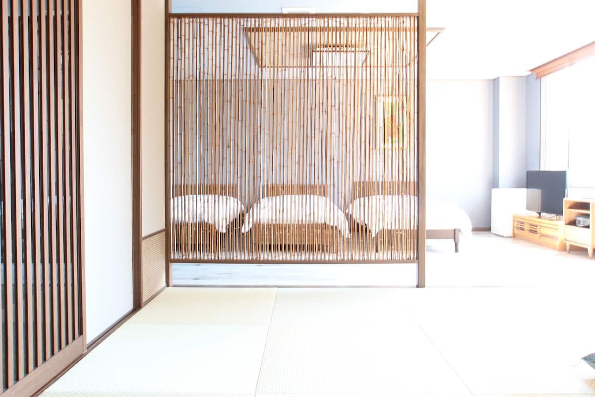 A traditional Japanese-style room with tatami flooring, a shoji screen, and a bed with white bedding.