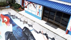 Un bâtiment orné d’une fresque représentant un grand oiseau et une personne tendant la main.