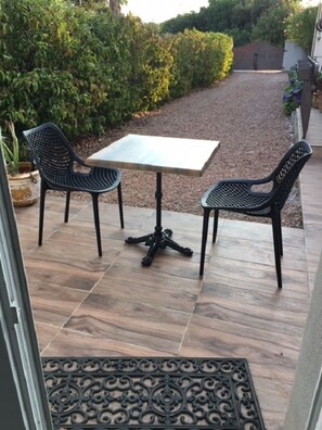 Une terrasse extérieure avec une table et deux chaises, entourée d’un jardin et d’une clôture en bois.