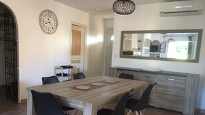 A dining area with a wooden table and black chairs, a clock on the wall, and a kitchen with a large mirror.