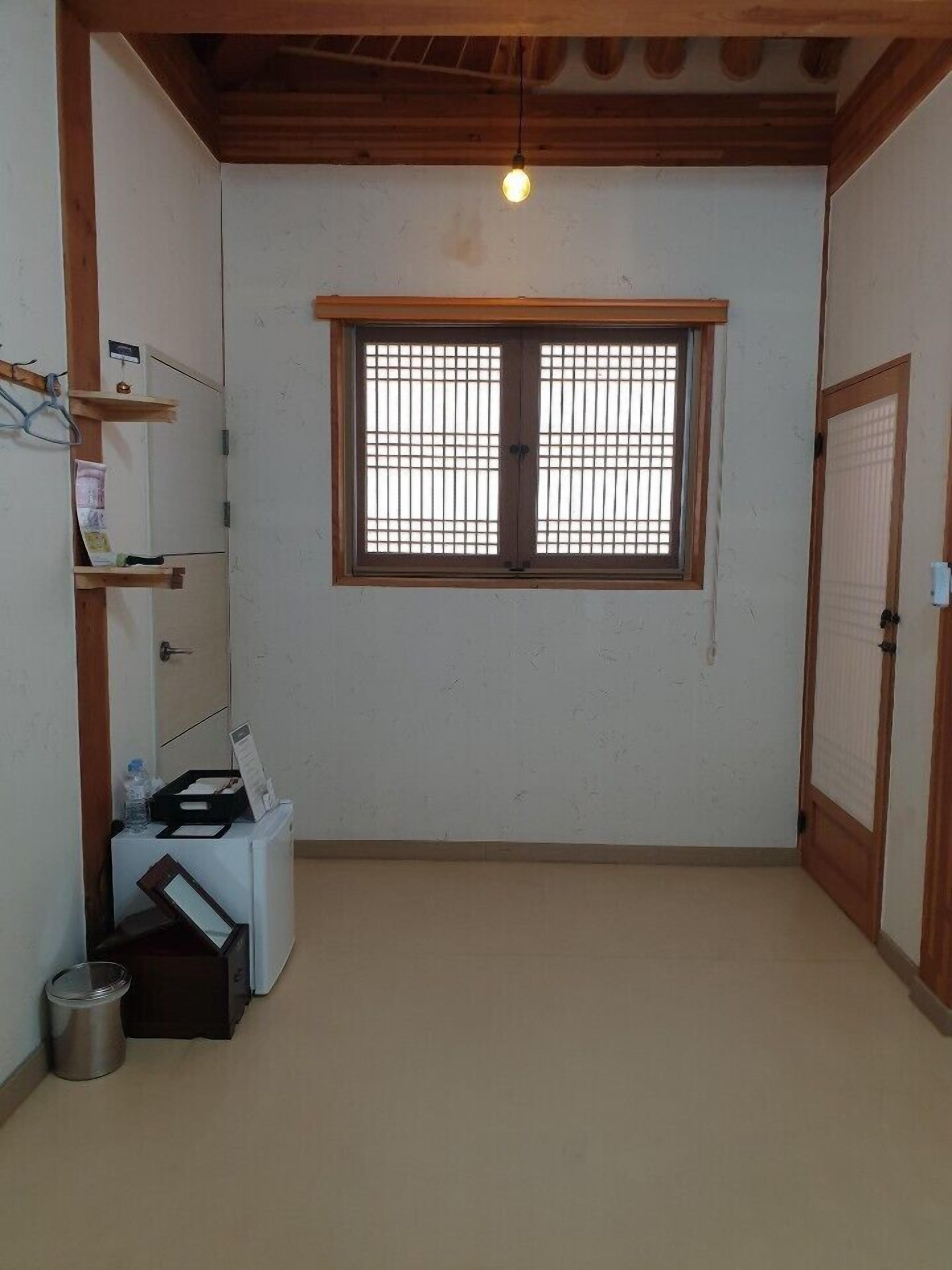 Una habitación pequeña y limpia, con un único ventanal, vigas de madera en el techo y una lavadora blanca.