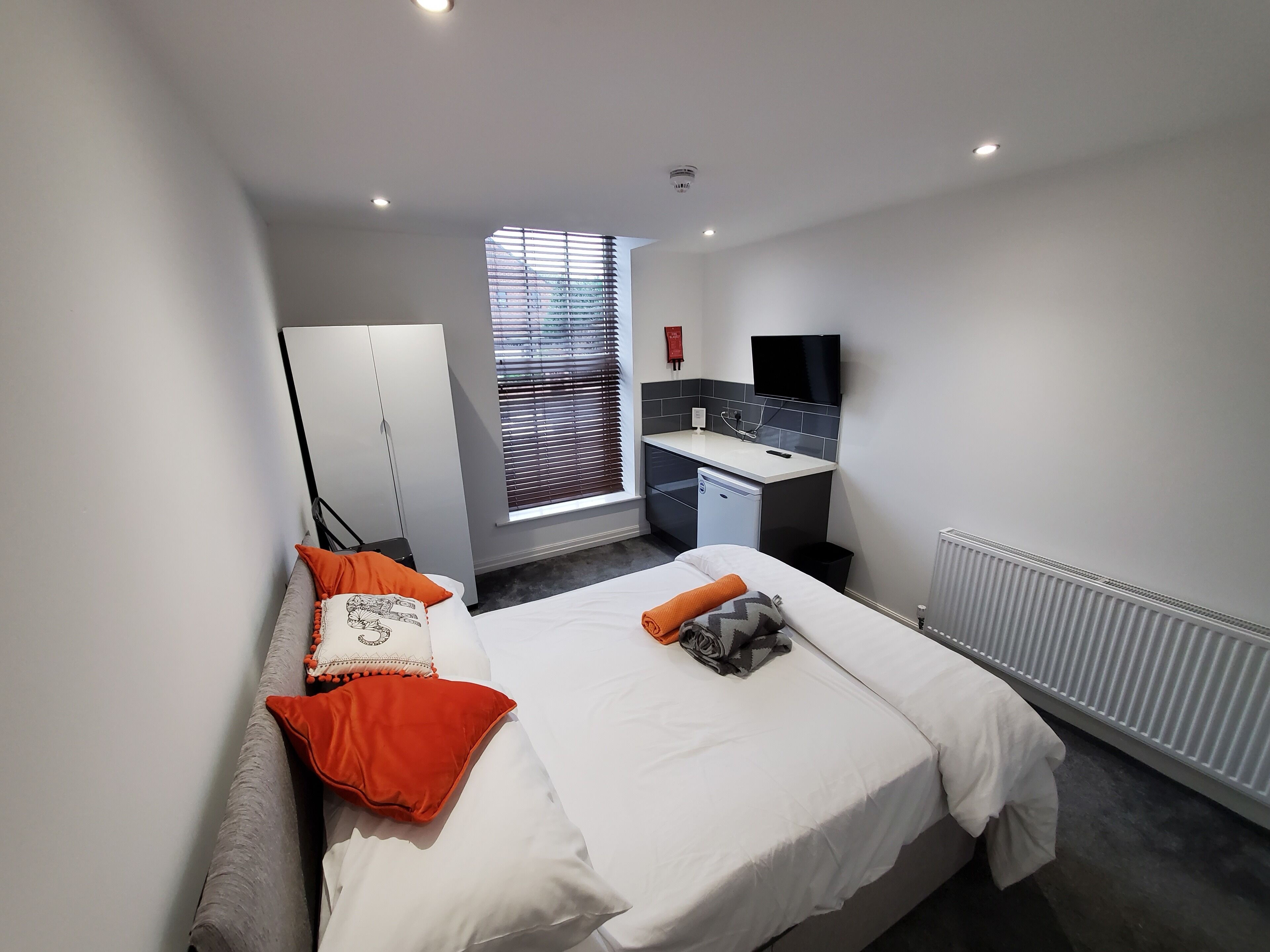 A modern hotel room with a bed, a desk, a TV, and a window with blinds.