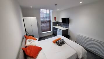 A modern hotel room with a bed, a desk, a TV, and a window with blinds.
