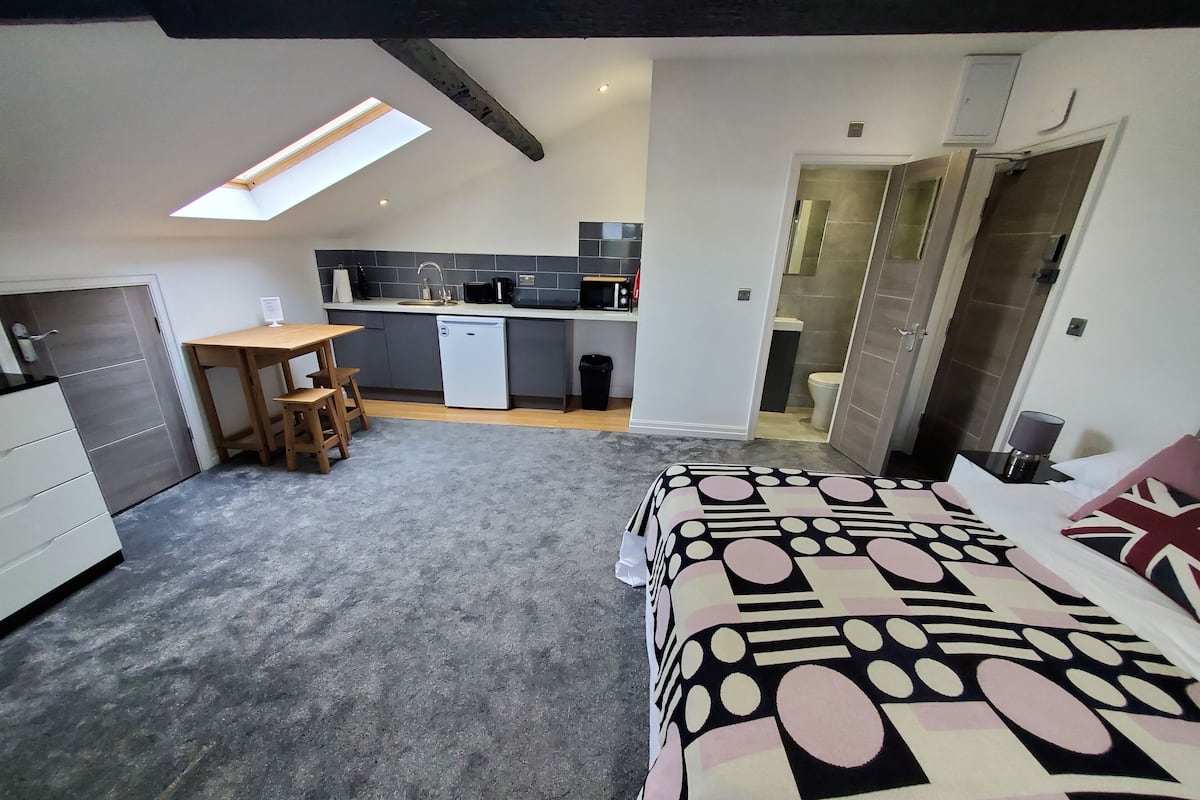 A bedroom with a bed, a desk, and a kitchenette.