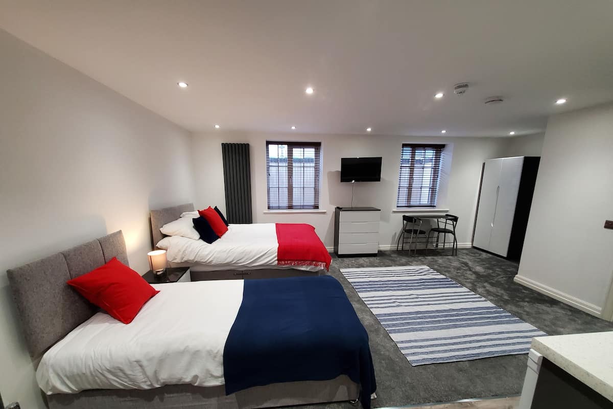 A modern hotel room with two beds, a desk, a chair, a TV, and a wardrobe.