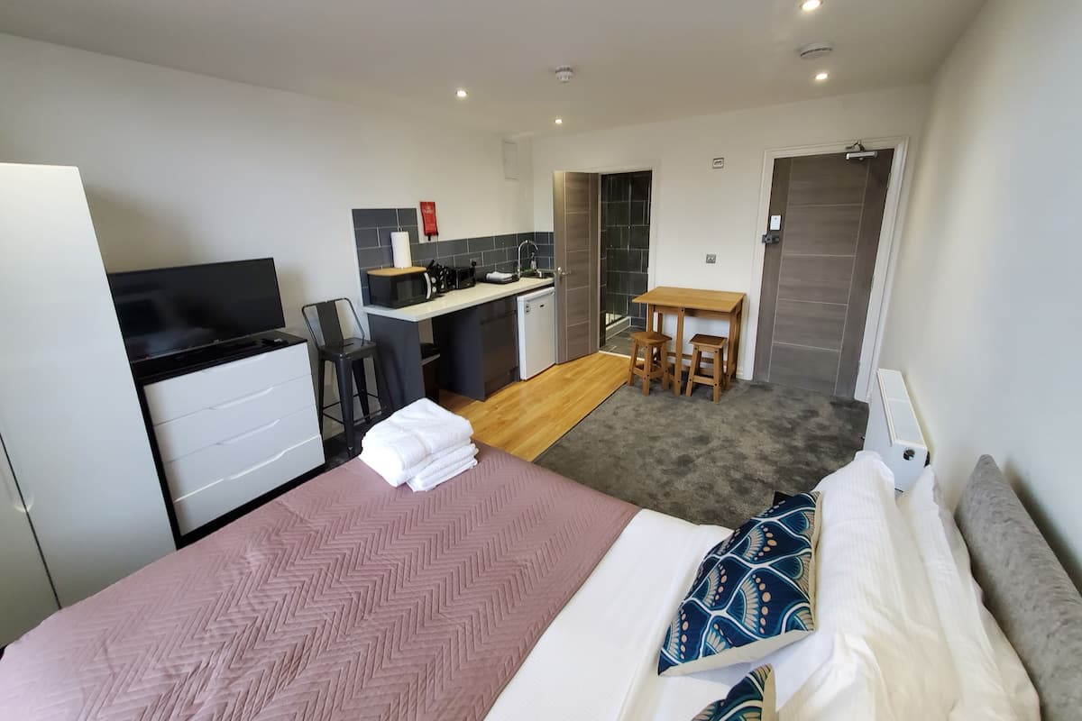 A compact hotel room with a bed, a small kitchenette, a dining area, and a bathroom.