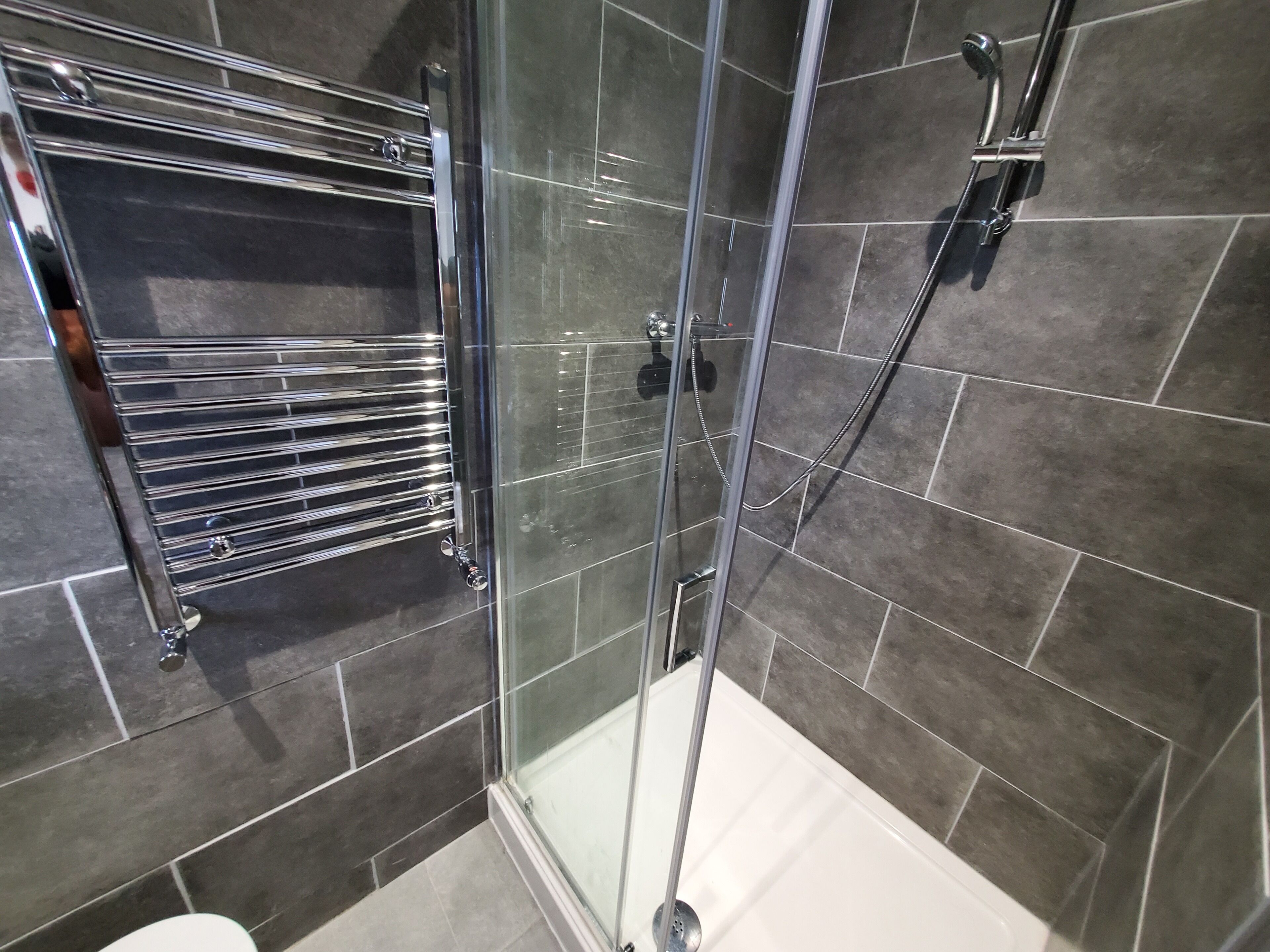 A glass-enclosed shower with a chrome towel rack and a handheld showerhead.