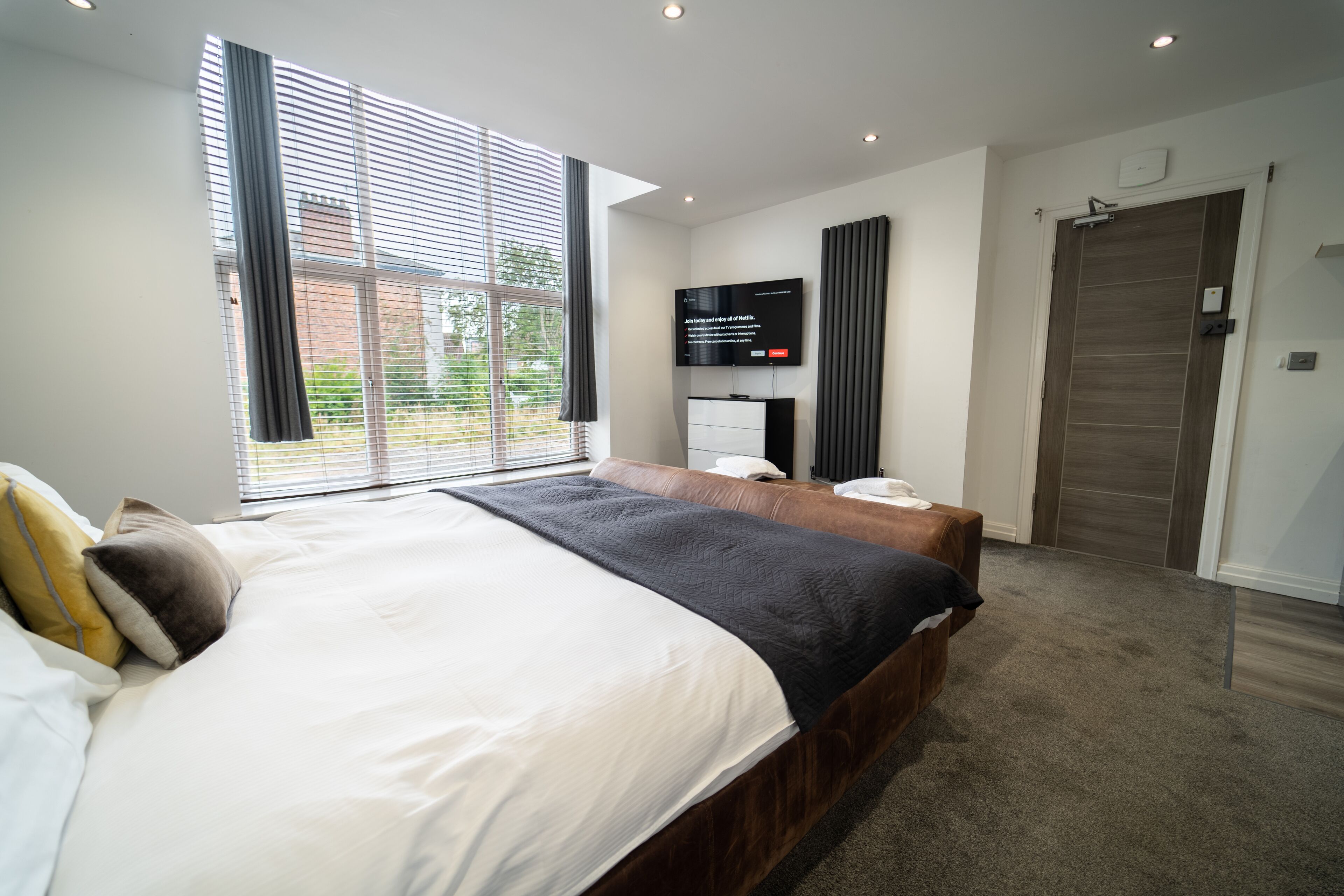 Ein modernes Schlafzimmer mit einem großen Bett, einem Flachbildfernseher, einem Schreibtisch und einer Schiebetür.