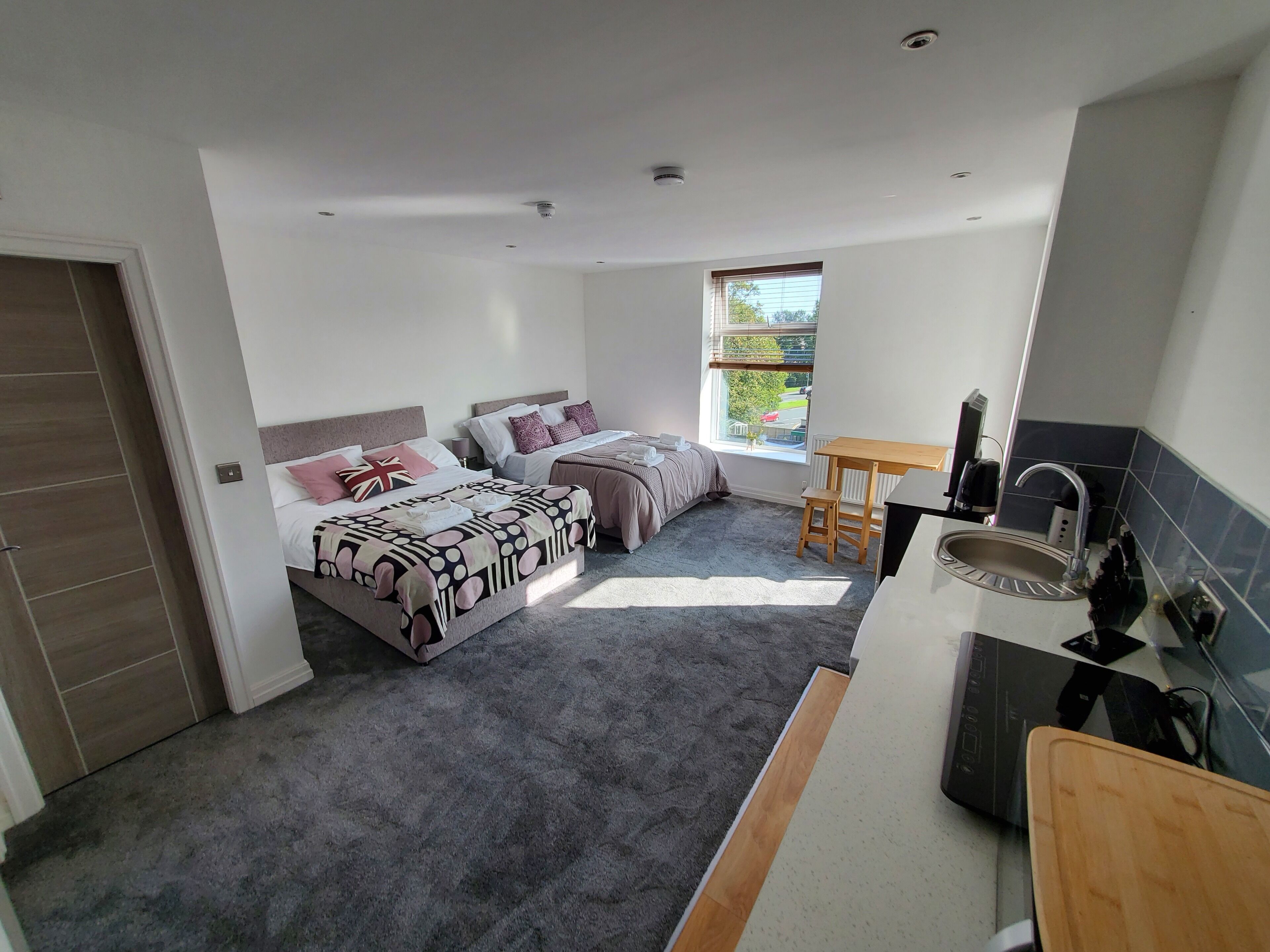 A compact bedroom with two beds, a small table, and a kitchenette.