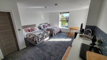 A compact bedroom with two beds, a small table, and a kitchenette.
