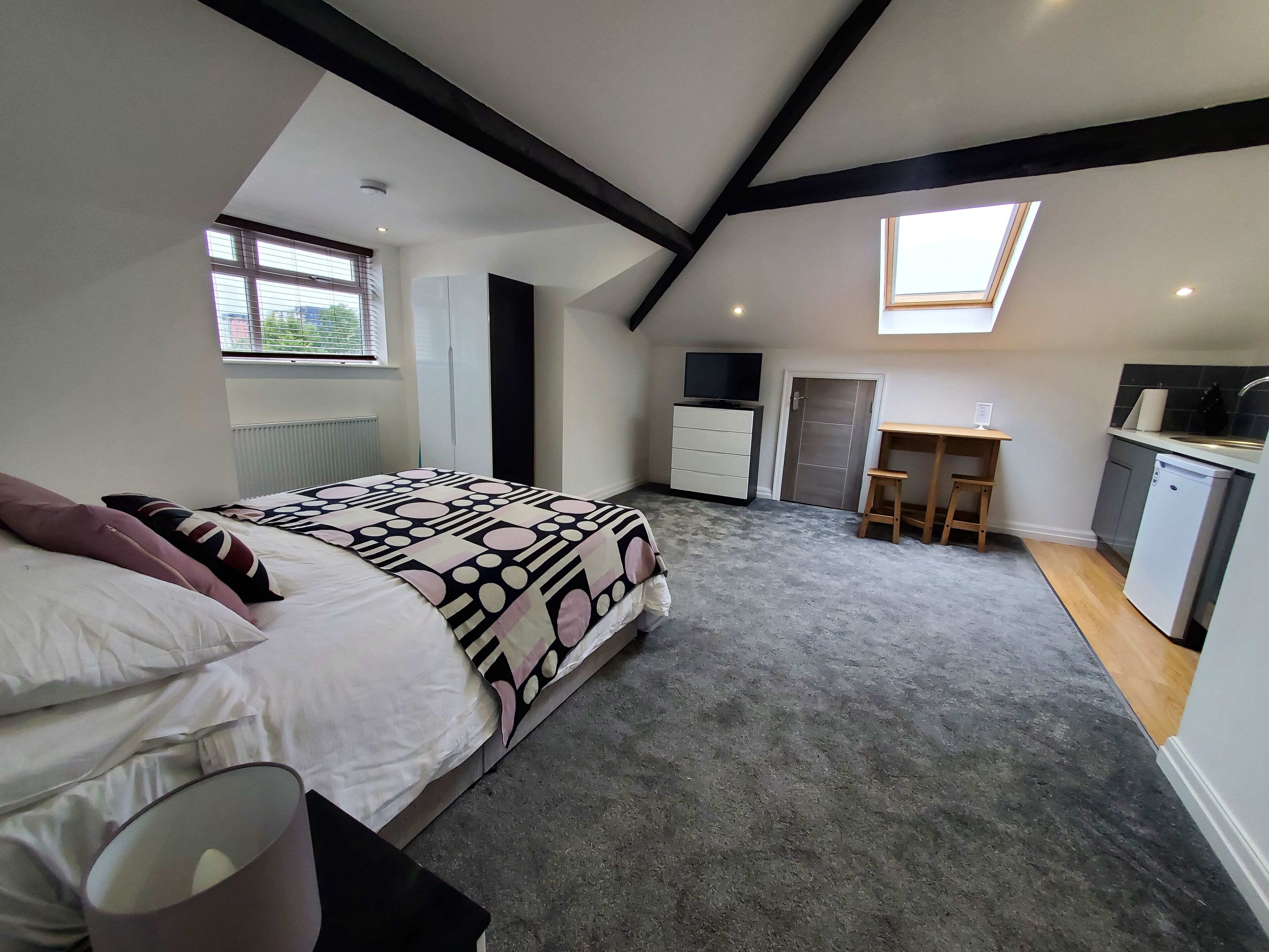 A bedroom with a bed, a desk, a wardrobe, a television, and a skylight.