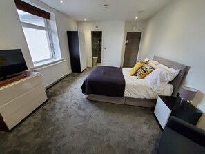 Quarto com uma cama, televisão em uma cômoda, janela e porta que dá para um banheiro.