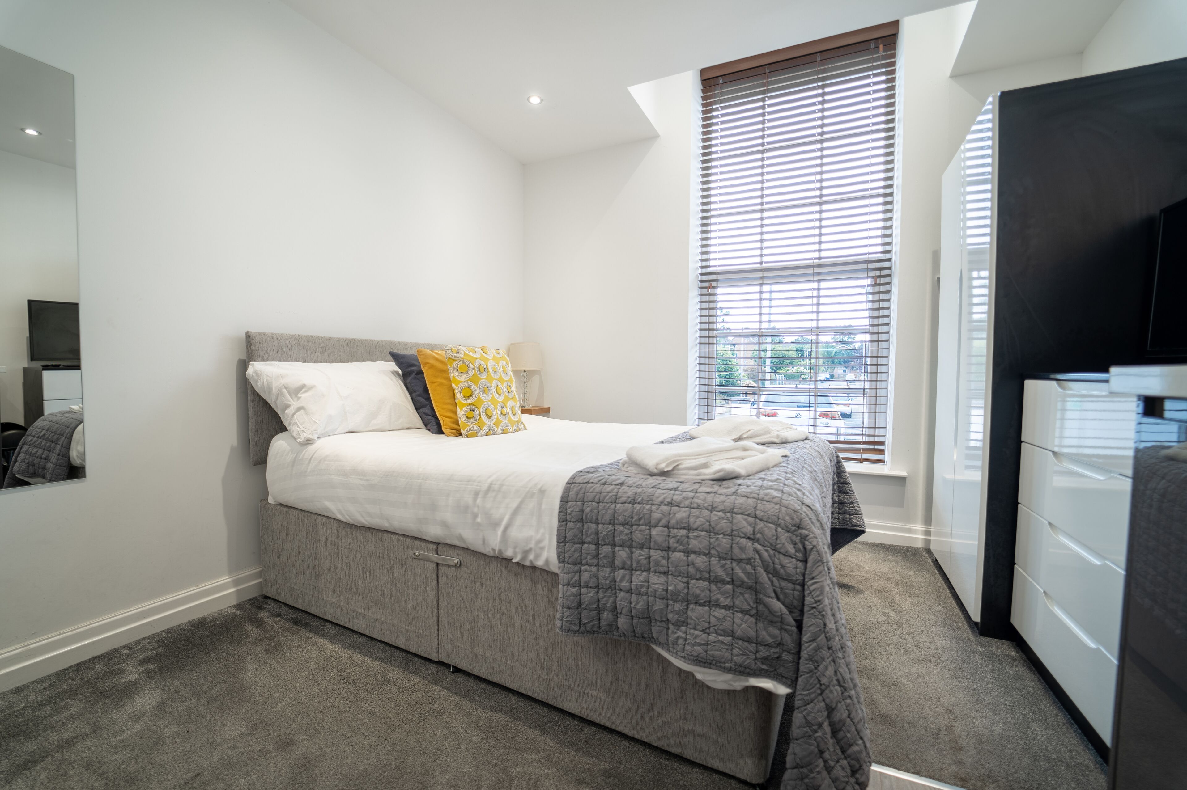 Een moderne slaapkamer met een bed, een dressoir en een raam met jaloezieën.