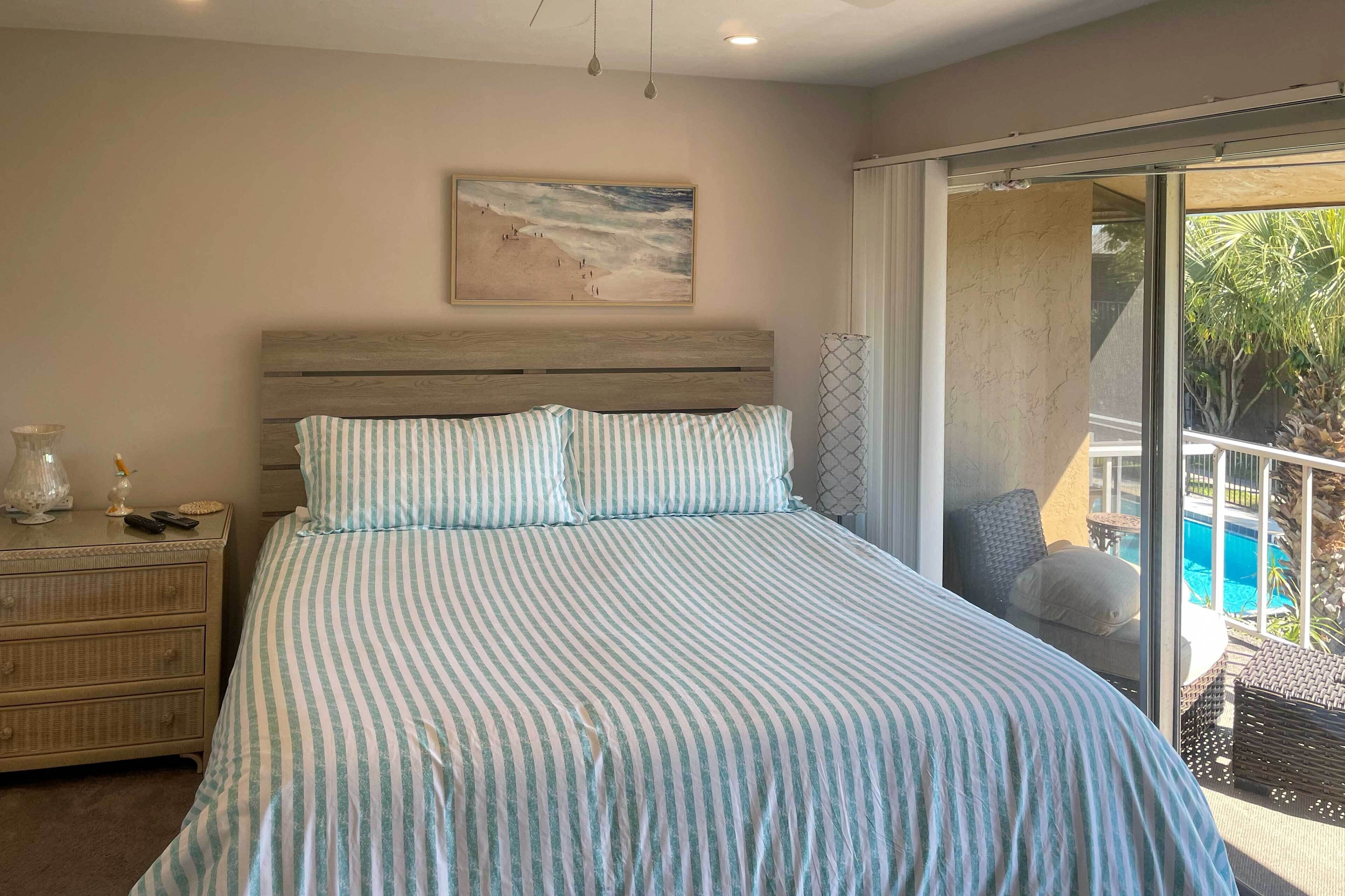 Une chambre avec un grand lit, une tête de lit en bois, une table de chevet avec une lampe, et une vue sur une piscine par une porte-fenêtre coulissante.