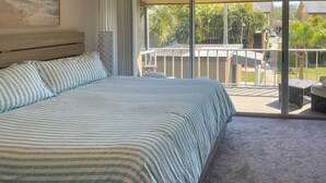 A bedroom with a large bed, a view of a balcony with outdoor furniture, and a painting on the wall.
