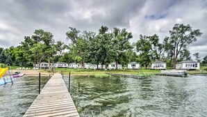Un muelle de madera que conduce a un lago, con varias cabañas pequeñas y un bote amarrado a la derecha.