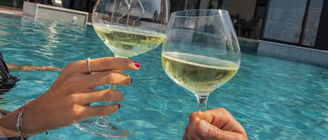 Dos manos sosteniendo copas de vino sobre una piscina.