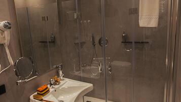 A modern bathroom with a glass-enclosed shower, a sink with a mirror, and a hairdryer on the wall.