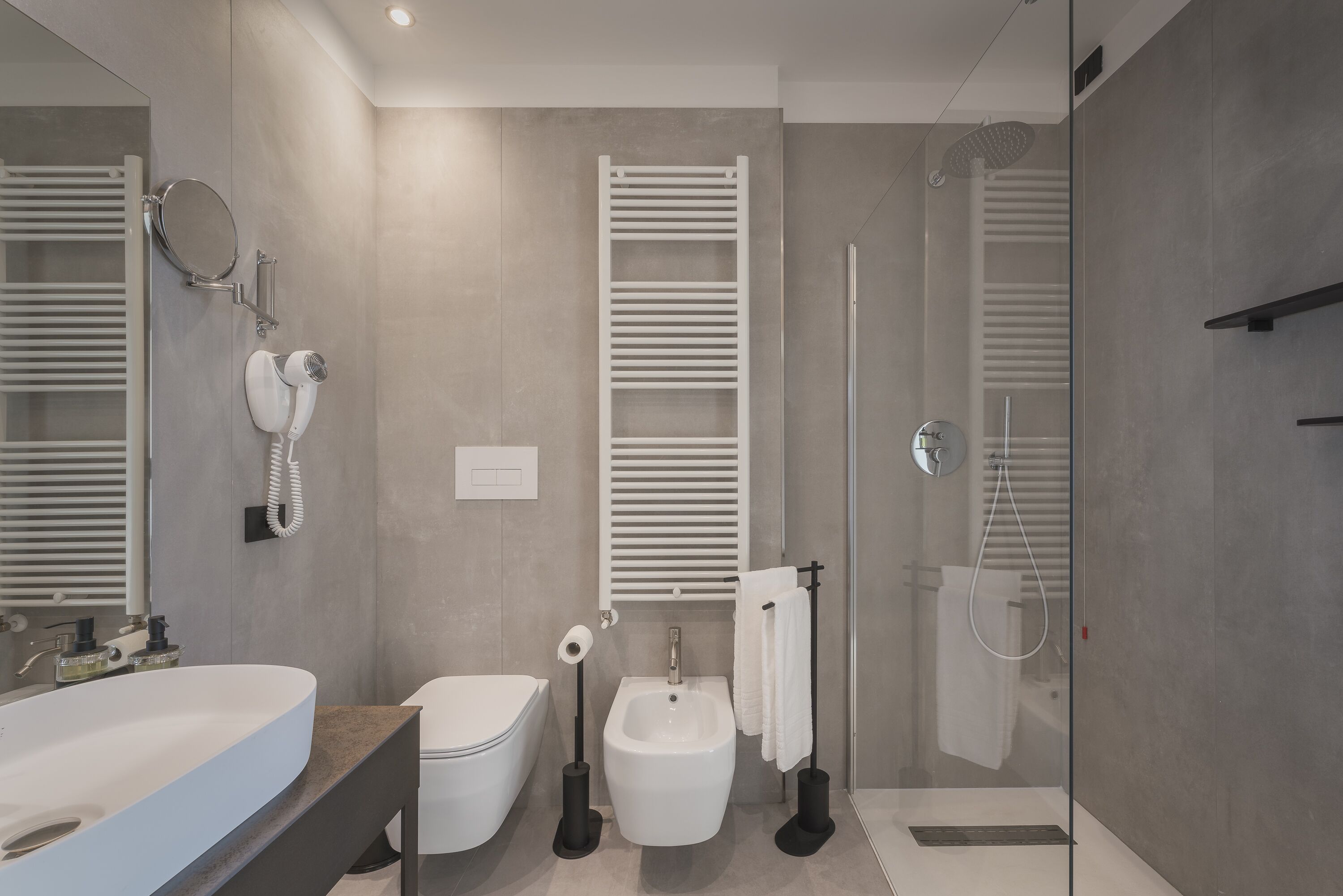 Un baño moderno con un lavamanos grande, inodoro, bidé y zona de ducha con mampara de vidrio.