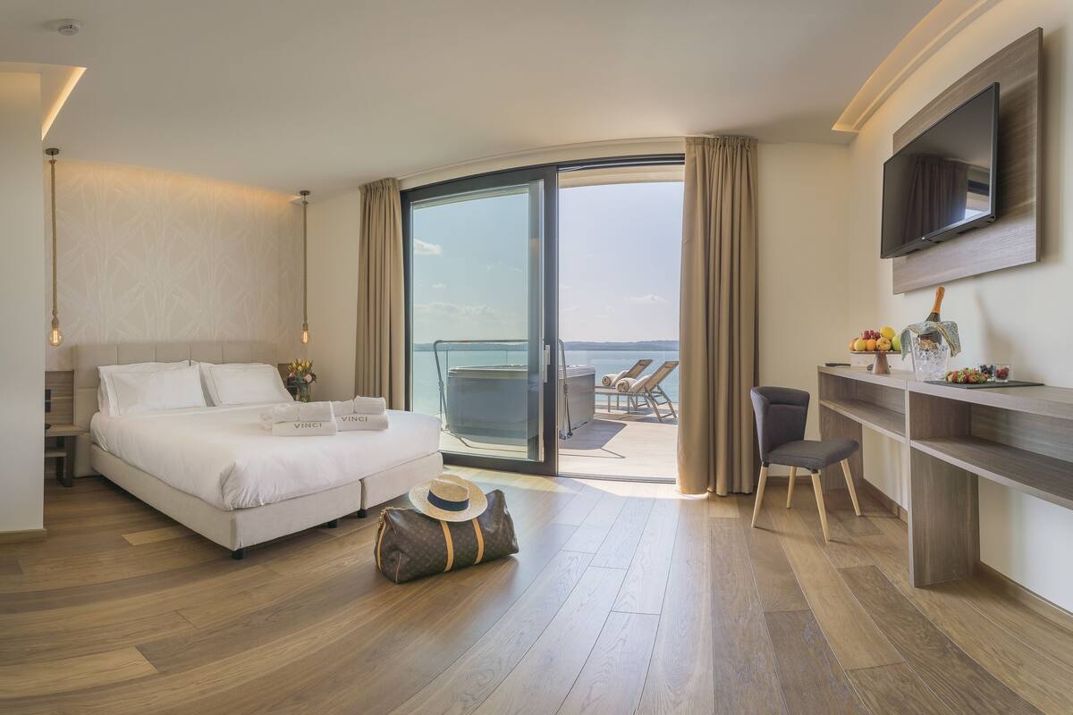 Habitación de hotel con una cama grande, un escritorio con silla, televisión y un balcón con vistas.