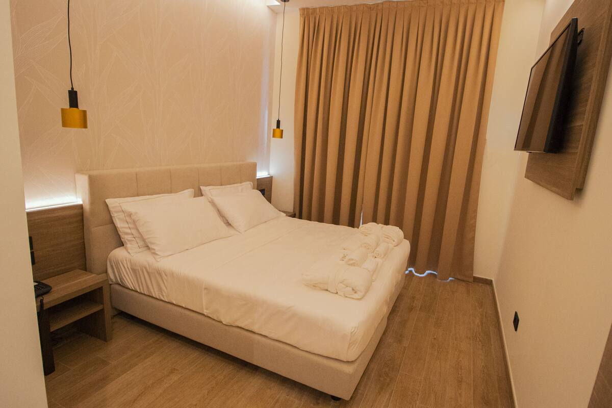Una cama bien hecha con sábanas blancas, un cabecero de madera y una mesita de noche con una lámpara.