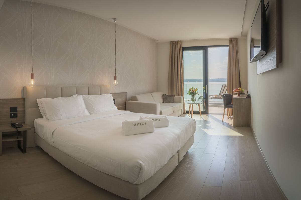 Habitación de hotel moderna con una cama grande, mesitas de noche, un escritorio y vistas al mar.