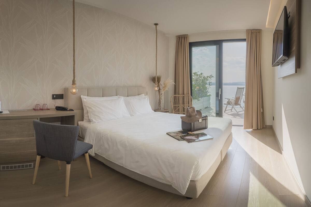 Habitación de hotel moderna con una cama grande, un escritorio con una silla, un televisor montado en la pared y vistas al exterior.