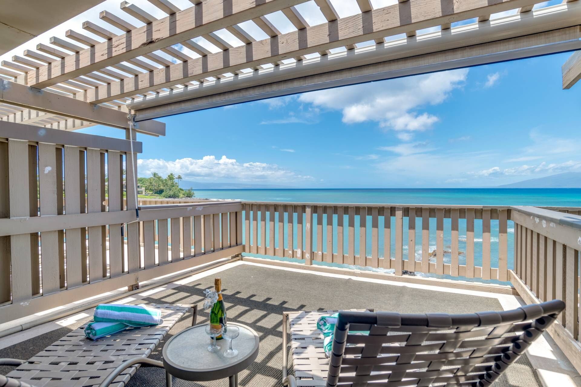 Un balcon avec vue sur l’océan, une table avec une bouteille et des verres, et deux fauteuils de relaxation.