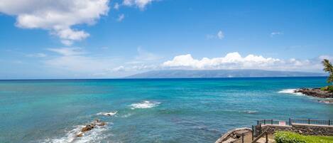 A coastal view with clear skies, turquoise waters, rocky shoreline, and a wooden staircase leading to a viewing platform.