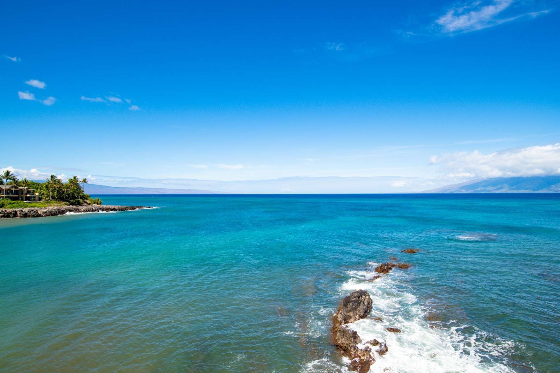 A coastal view with clear turquoise waters, a rocky shoreline, and a distant mountain range.