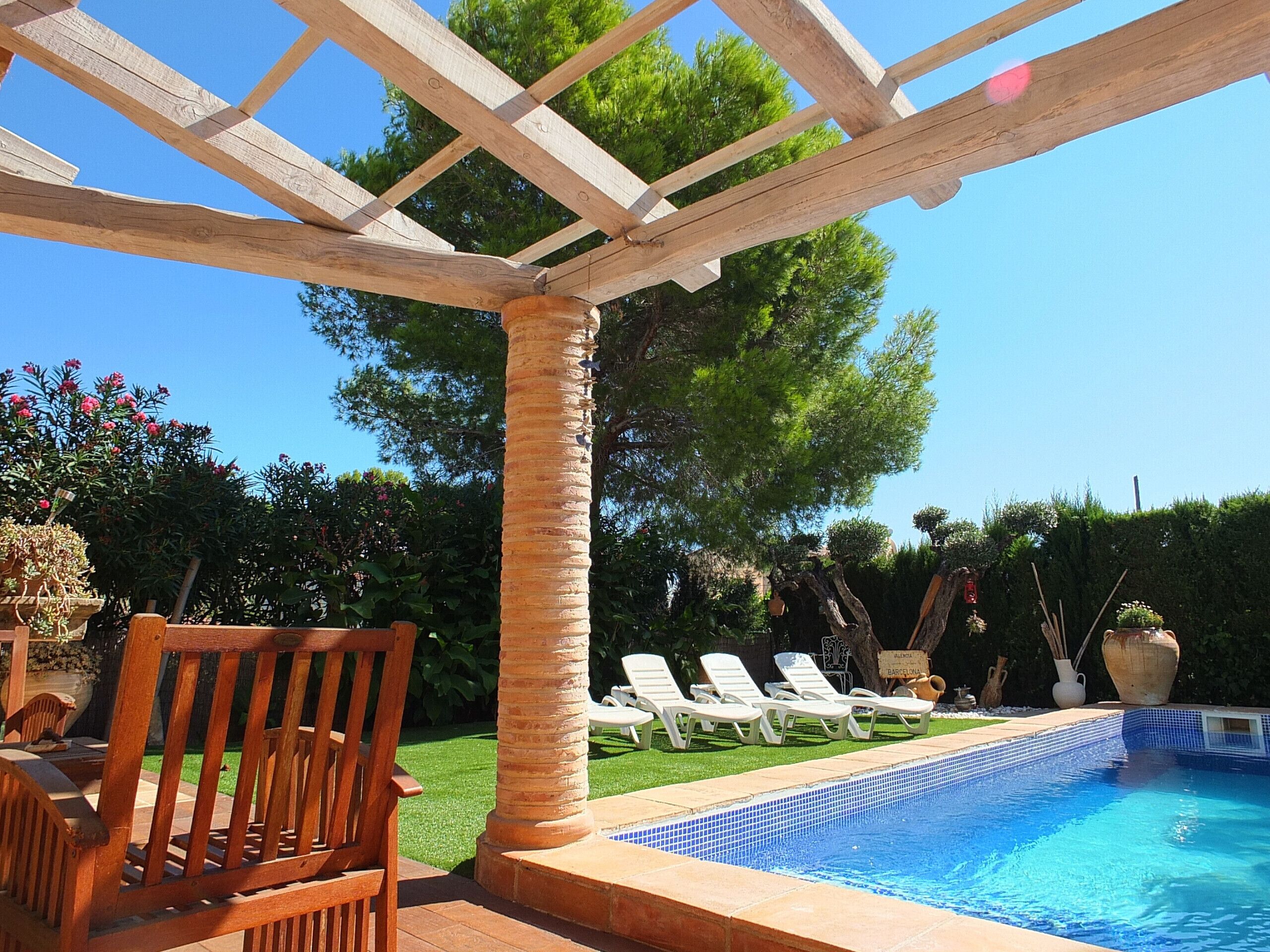 A pool area with a pergola, lounge chairs, and a wooden deck.