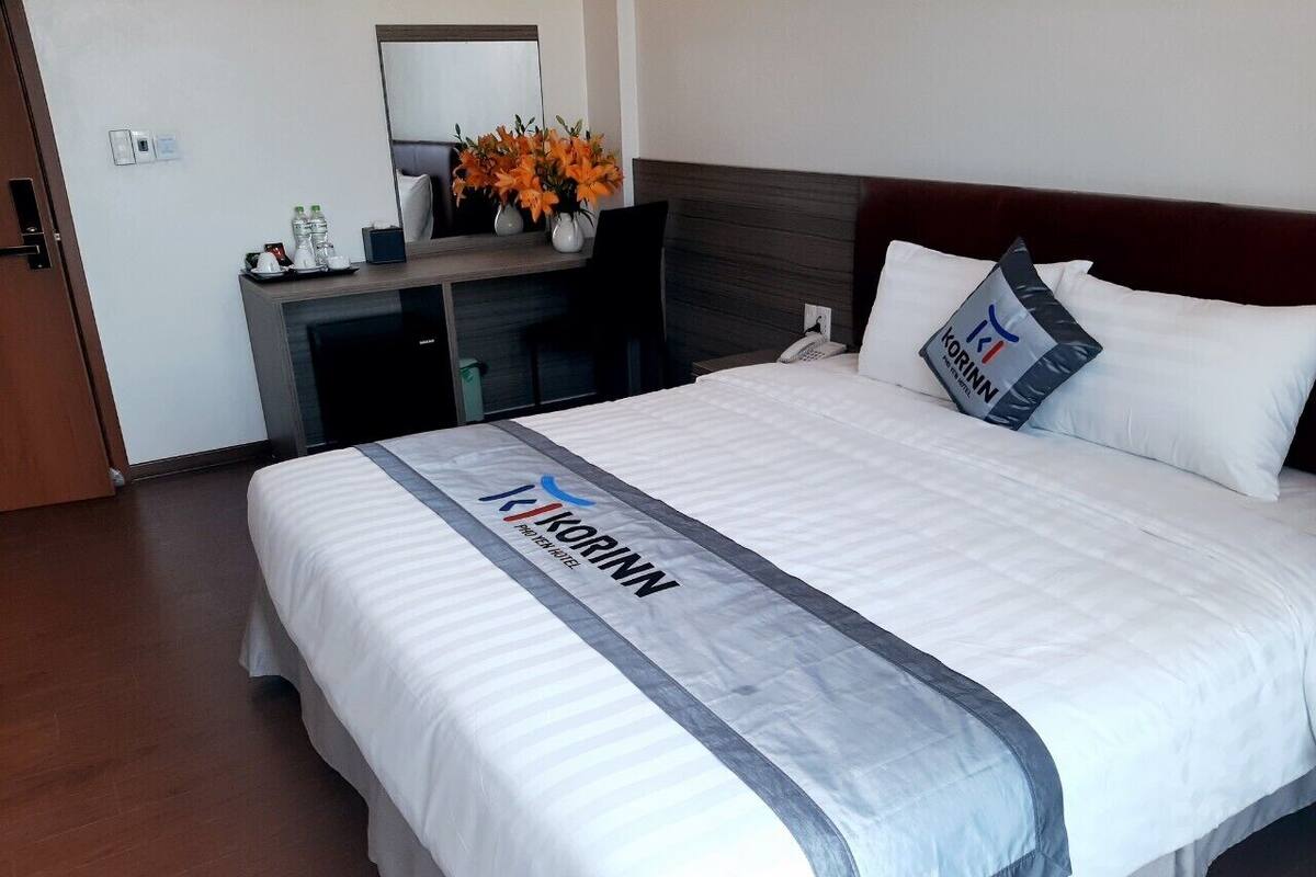 Ein Hotelzimmer mit einem großen Bett, einem Schreibtisch mit Stuhl, einem Spiegel und einer Blumenvase.