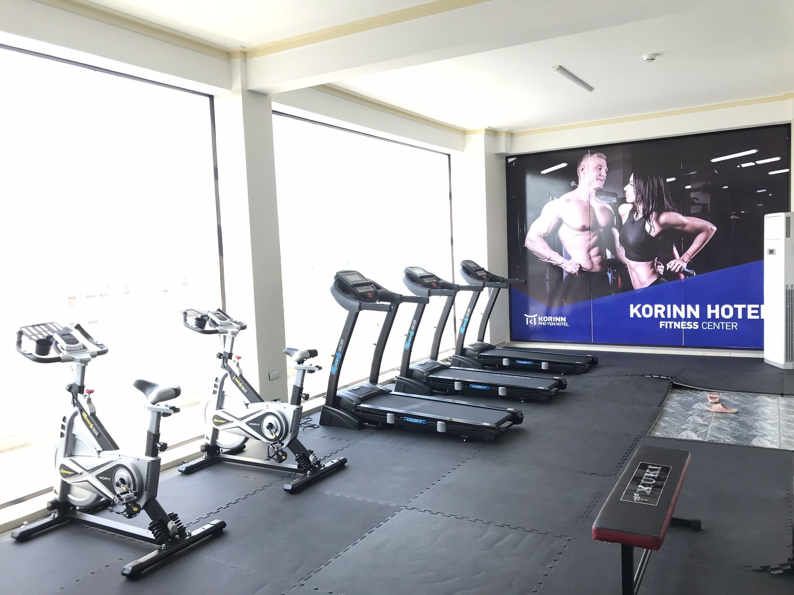 Un gimnasio con cintas de correr, bicicletas estáticas y una máquina de remo.