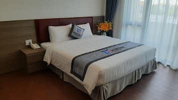 Una habitación de hotel con una cama, una mesita de noche con un teléfono y una ventana con cortinas.