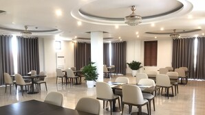 Une salle de conférence spacieuse, dotée de plusieurs tables et chaises, d’un lustre et de grandes fenêtres avec des rideaux.