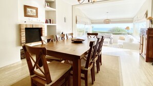 A dining area with a wooden table and chairs, a fireplace, and a view of the ocean.