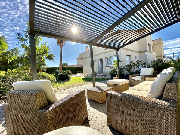 A covered outdoor seating area with wicker furniture and a view of a building in the background.